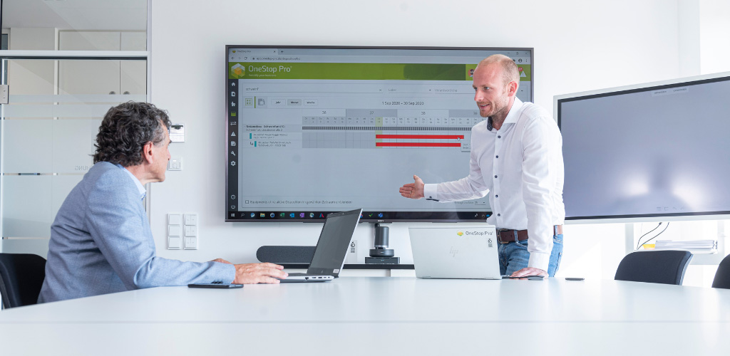 Zwei Personen sitzen in einem Besprechungsraum und arbeiten mit Laptops in einer Beratungs- und Schulungssituation.