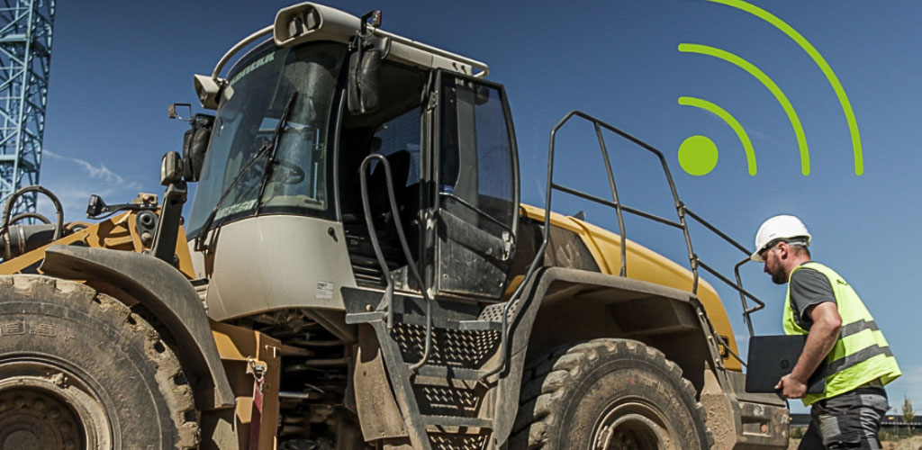 Baumaschine mit Arbeiter und Laptop auf Baustelle, Telematik- und Tracking-Signal visualisiert